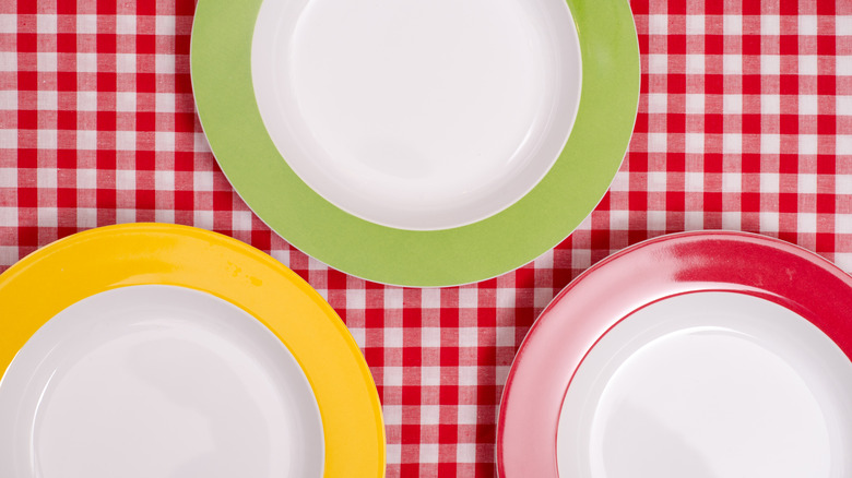 Three white plates — with red, green, & yellow rims — on white & red checkerboard pattern table