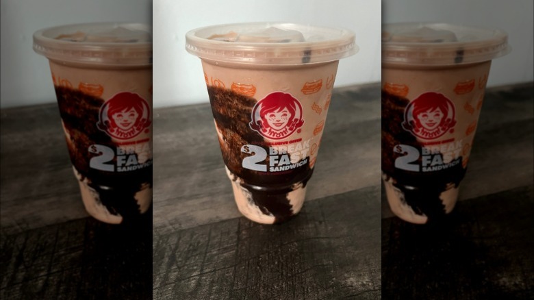 Wendy's frozen dessert in plastic cup on dark wooden table against white wall background