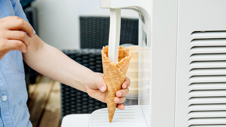 Child's hand holding ice cream cone, filling it with soft serve ice cream
