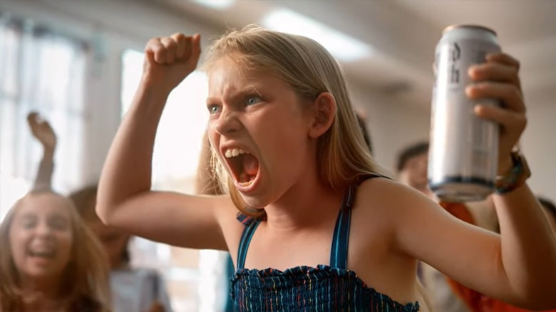 Girl yells, one fist up and a can of Liquid Death in her other hand 