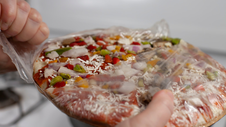 Hand opening a frozen pizza