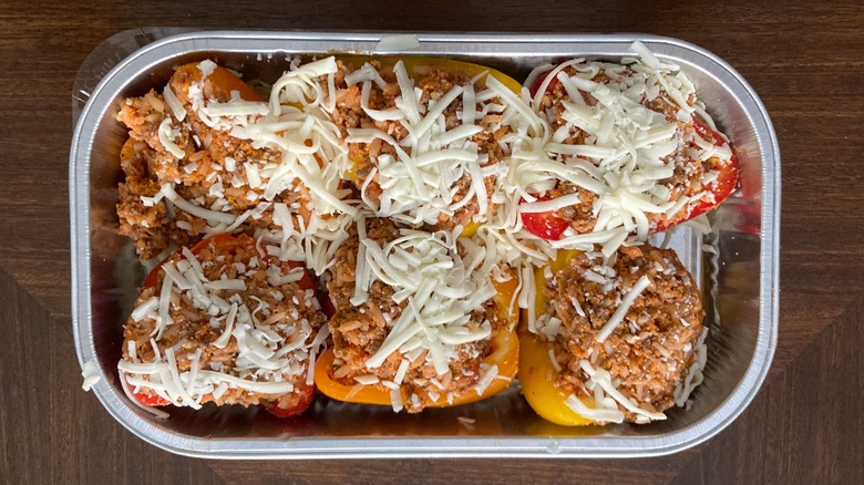 Metal tray with premade stuffed peppers topped with cheese sitting on table.