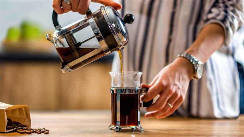 Person pouring French press coffee in small carafe