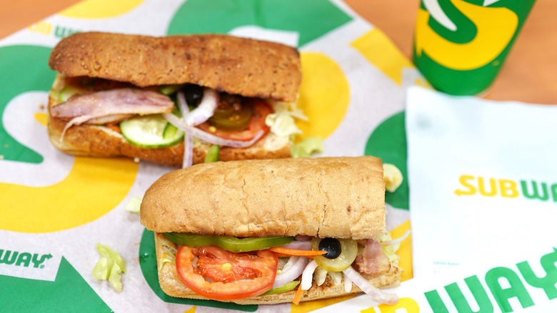 Two Subway sandwiches on Subway paper with a paper cup