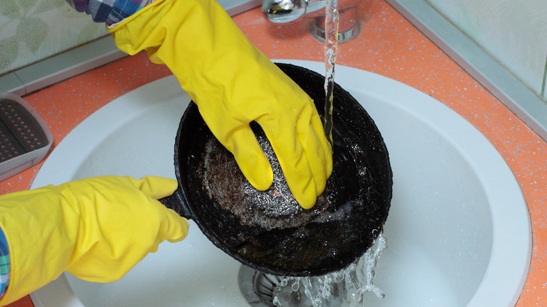Hands in yellow rubber gloves cleaning pan