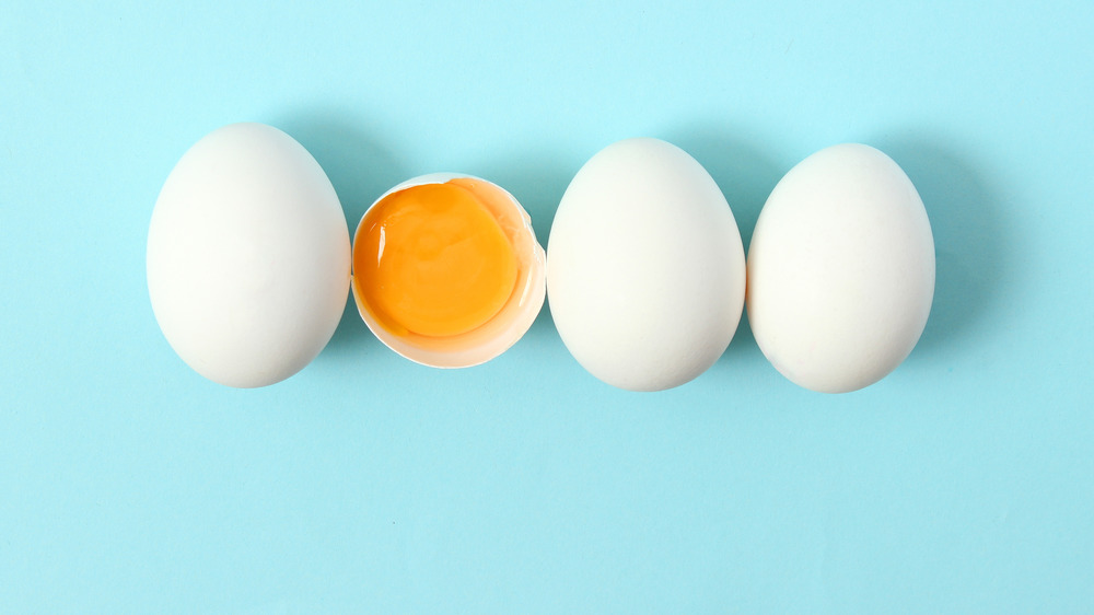 Three whole white eggs and one broken egg with yolk