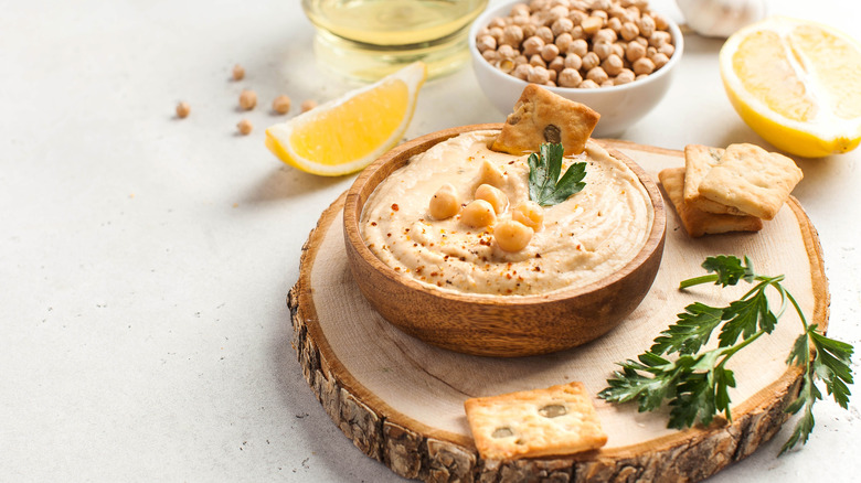 Hummus in a wooden bowl surrounded by chickpeas, lemons, and olive oil