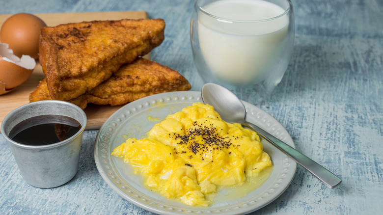 Scrambled eggs with a tin of maple syrup next to toast and milk