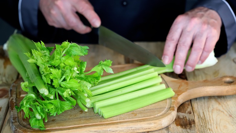 A person cutting celery on a cutting board