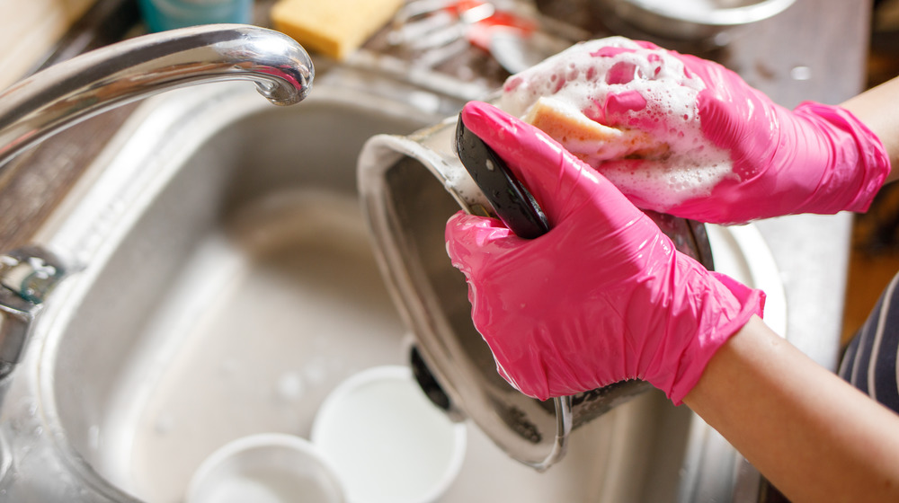 Person cleaning pot with pink gloves on