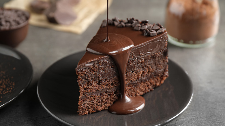 Melted chocolate being poured over a slice of chocolate cake