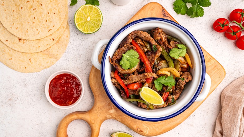 beef fajitas served on a wooden board with tortillas on the side