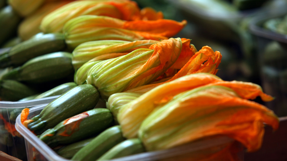 Fresh zucchini, with flowers attached, on display at a farmer's market.