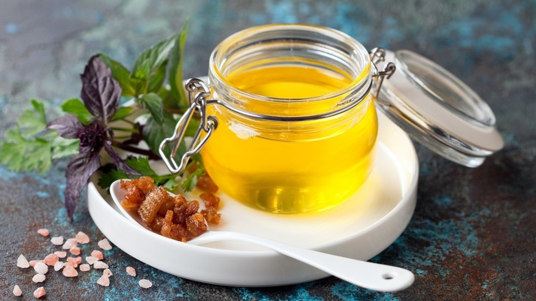 jar of liquid duck fat on a white plate with duck fat on a spoon