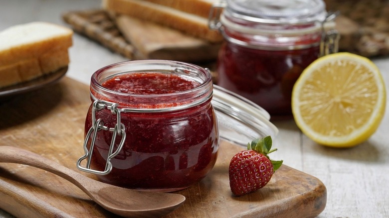 strawberry jam in a jar on a cutting board with wooden spoon