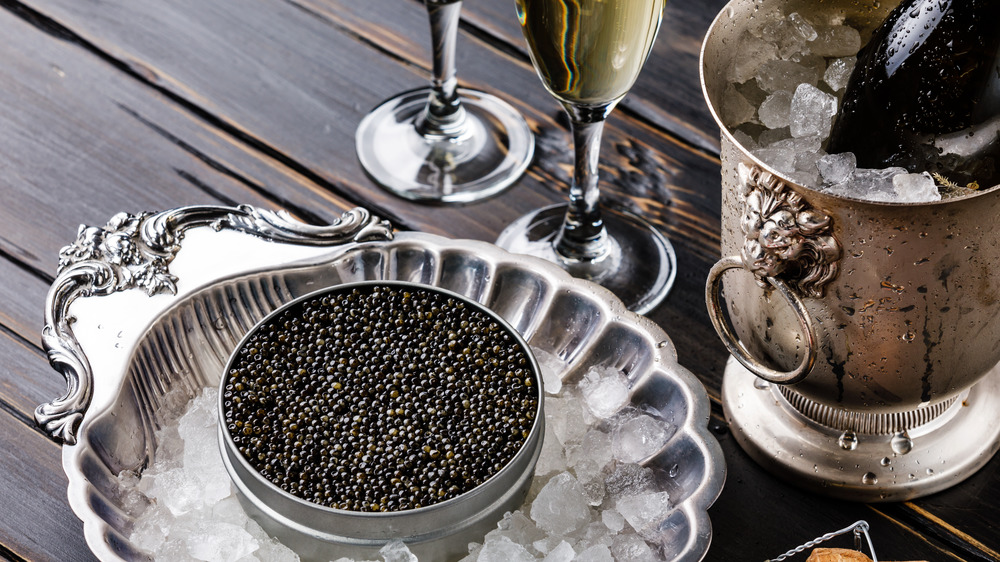 Tin of caviar on ice next to champagne bucket and two glasses of champagne