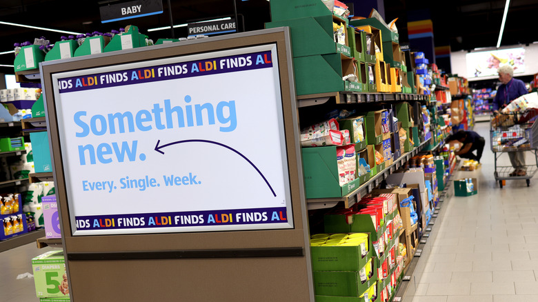 A promotional sign reminds shoppers of "Aldi Finds" in front of well-stocked Aldi aisles.