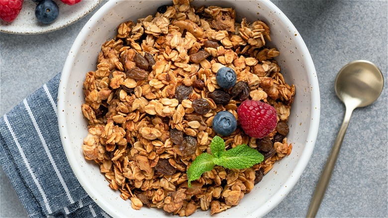 bowl of granola and a spoon with raisins, blueberries and raspberries as toppings