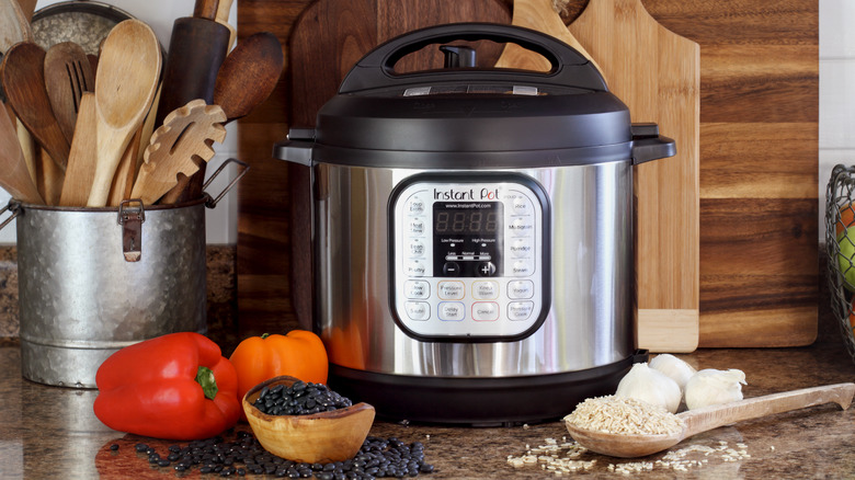 instant pot on kitchen counter next to peppers, beans, rice, garlic