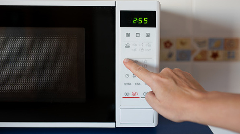 A hand pressing settings on a microwave oven