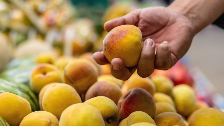 A hand picking up a peach at the grocery store
