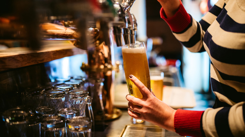 Bartender pouring beer into tall glass from tap.