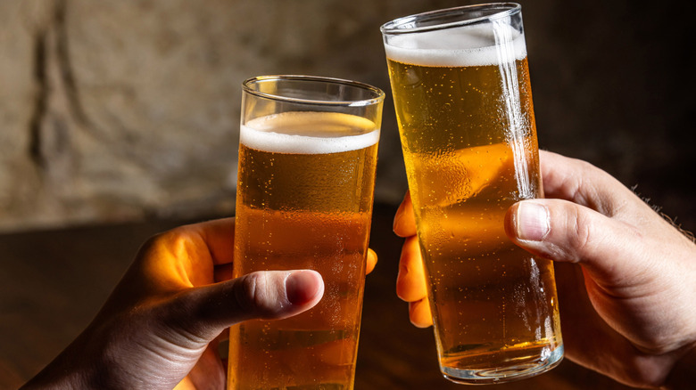 Two people toasting stange glasses of pilsner beer.
