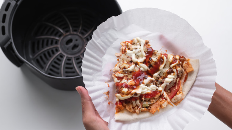 Hands holding leftover pizza on parchment paper