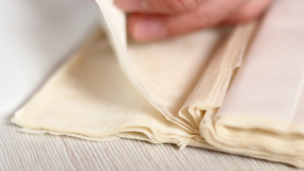 Phyllo dough on a counter with a hand lifting sheets of dough 