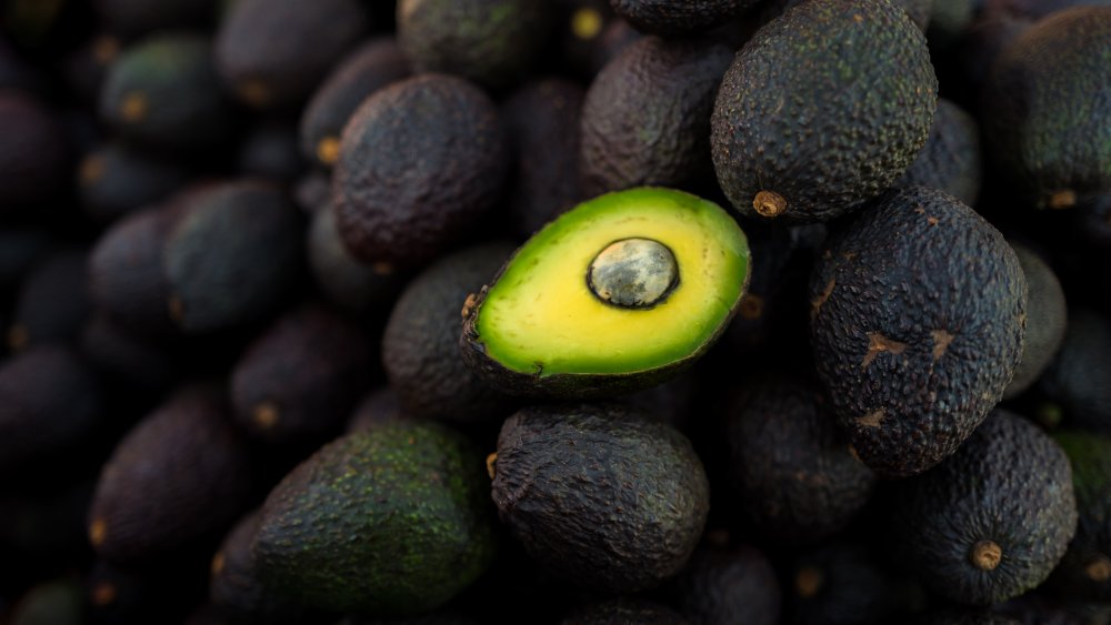 A bisected avocado lies upon its unharmed brethren.