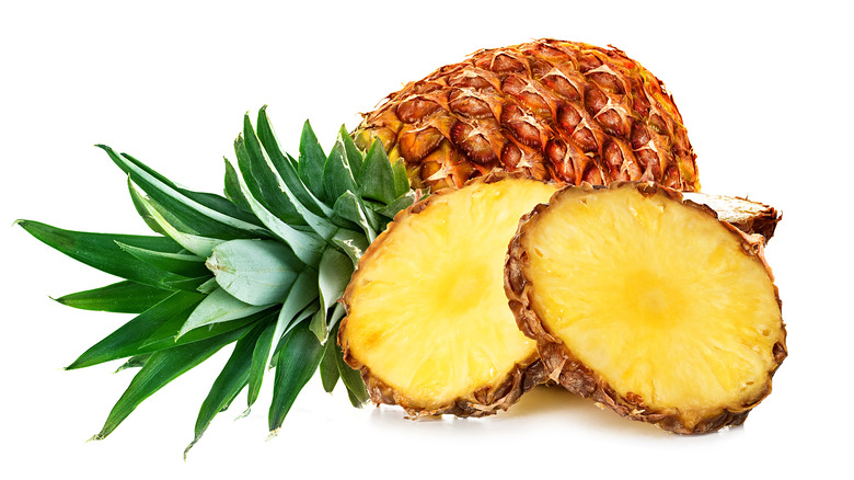 A whole pineapple next to cut up round slices