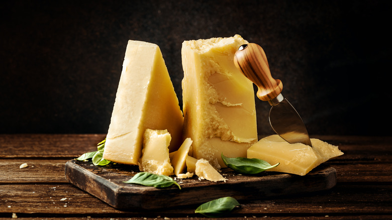 Blocks of parmesan cheese on a wooden board with basil leaves