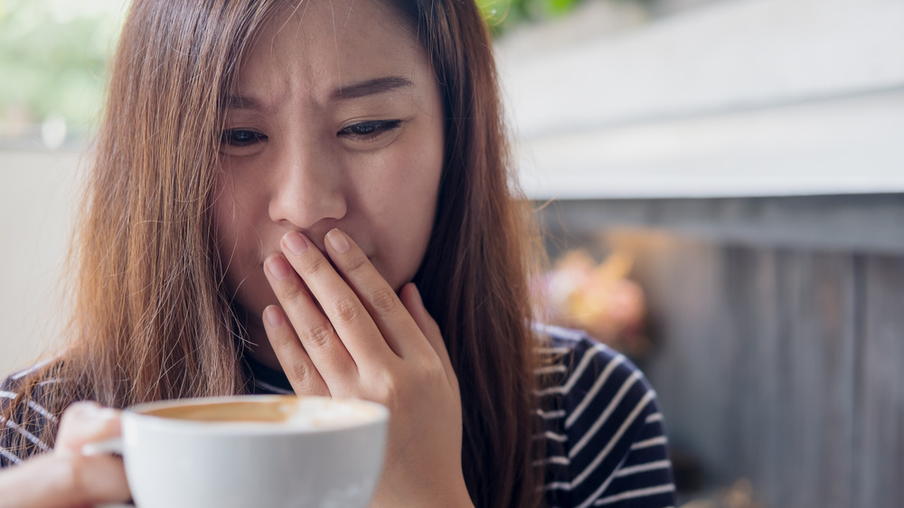 Woman holding coffee cup looking disgusted