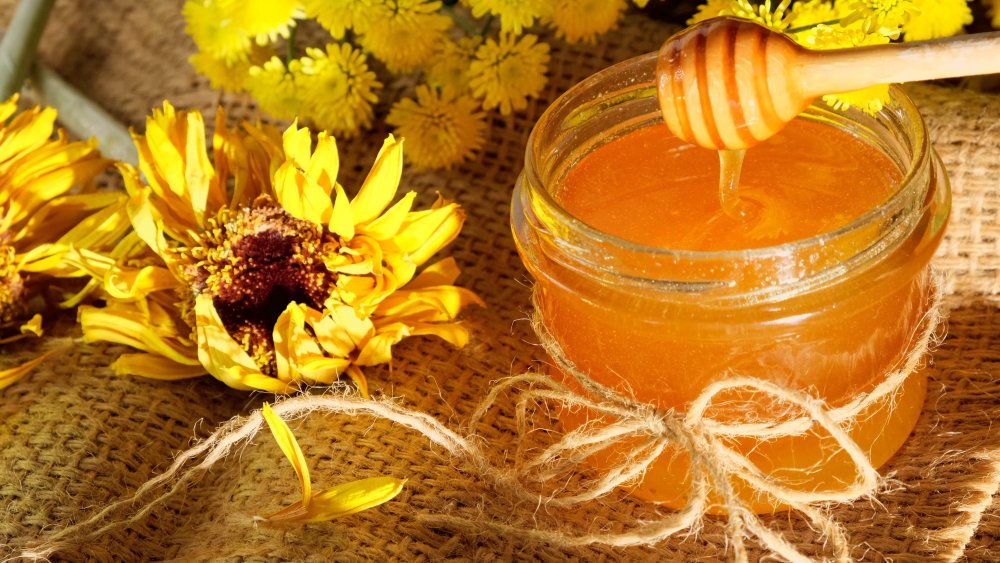 honey dripping into a jar with flowers on the side 