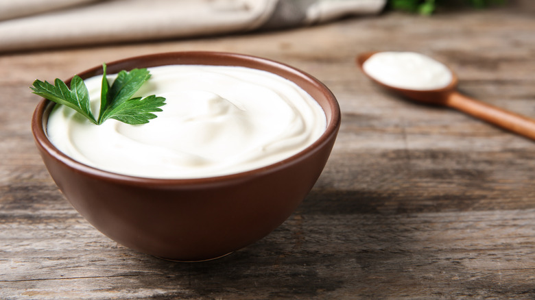 Sour cream in brown bowl on wood surface