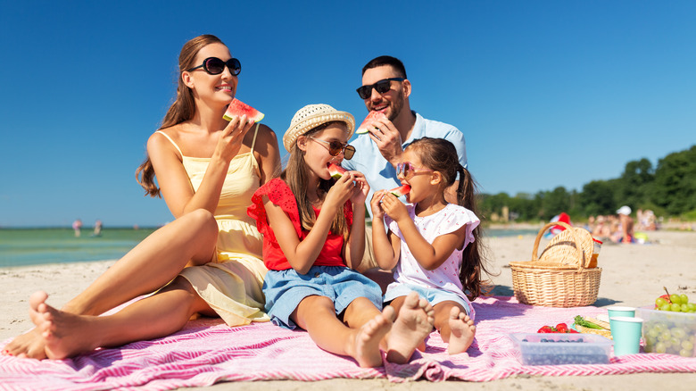 Family on a blanket eating food at the beach