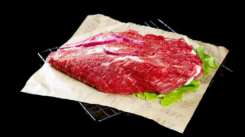 A large cut of raw beef brisket on parchment paper with a black background.