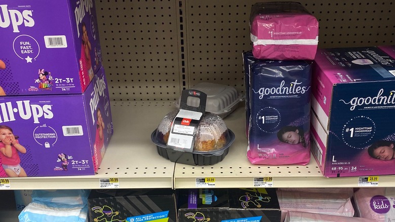 A rotisserie chicken on a shelf of diapers