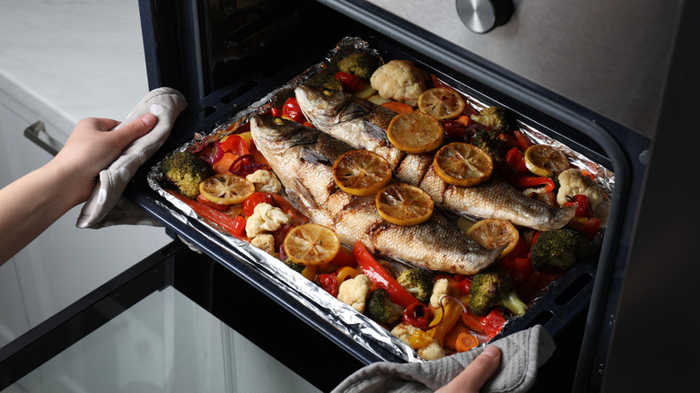 Whole fish being roasted with citrus slices and vegetables on aluminum foil