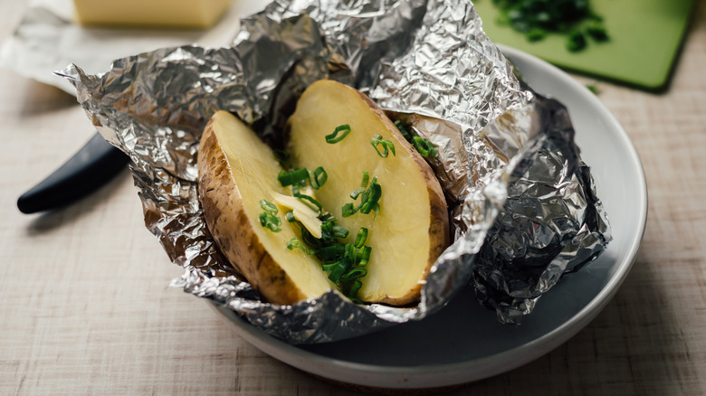 Baked potato with butter and chives in aluminum foil