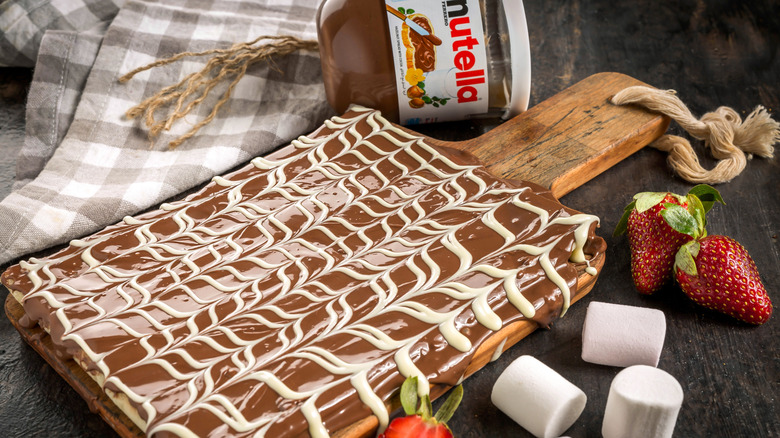 A crêpe spread with Nutella and marshmallow drizzle on a cutting board.