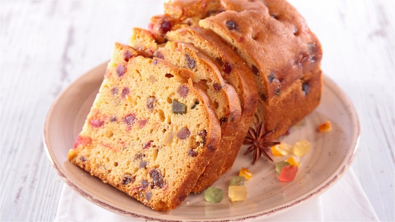 A sliced fruitcake with anise and candied fruit beside it