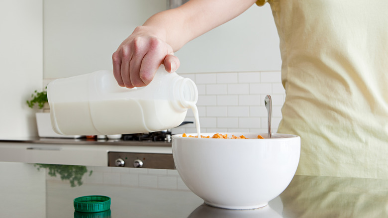 person pouring milk into bowl of cereal in kitchen