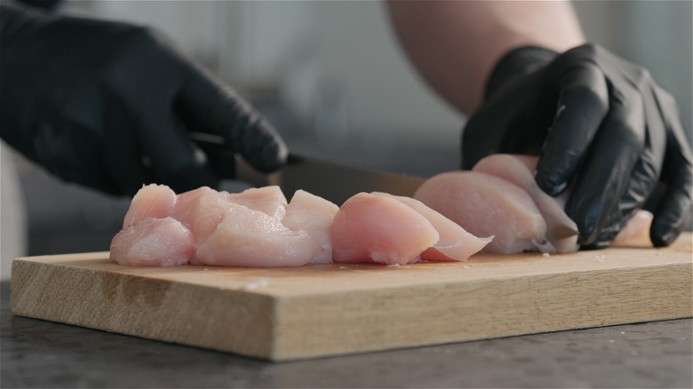 Person cutting raw chicken in black latex gloves