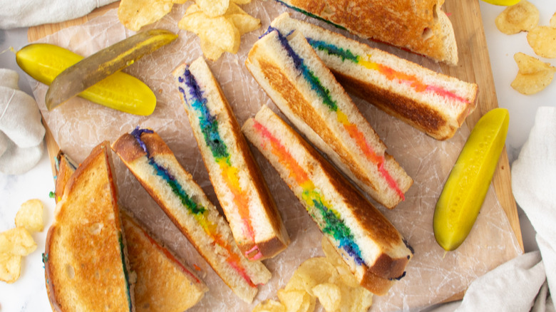 colorful rainbow grilled cheese halves stacked on board with pickle spears and chips
