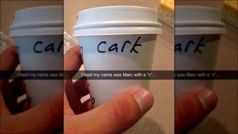 Hand holding Starbucks cup with "Marc" misspelled as "Cark."
