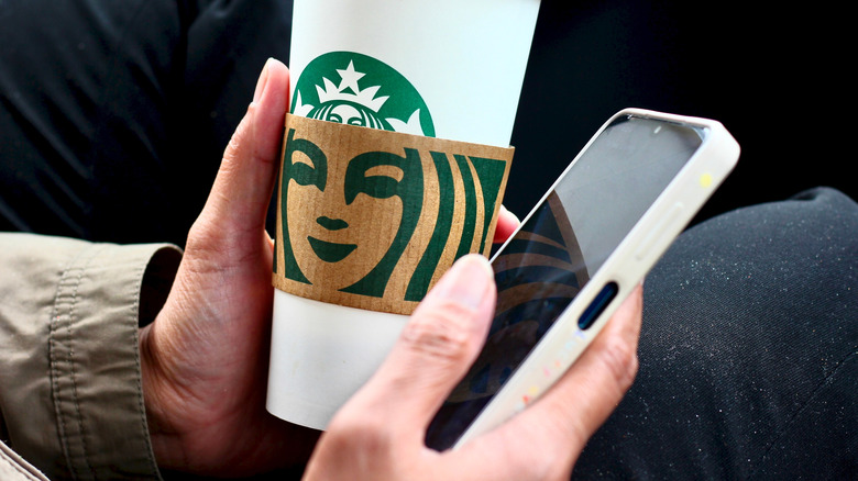 Person holding Starbucks cup in one hand and a smartphone in the other.