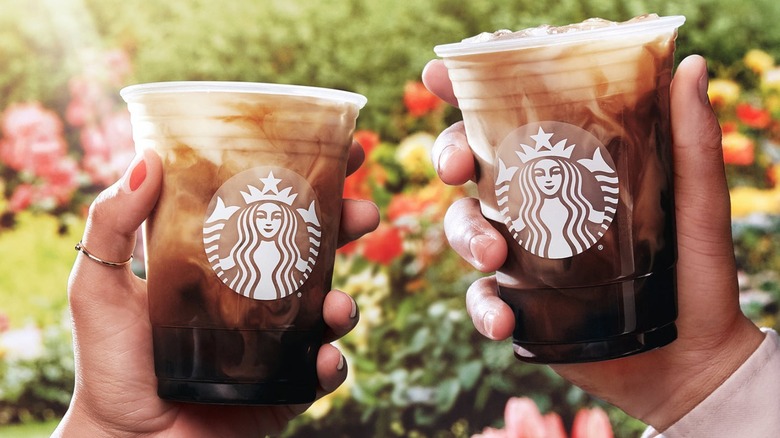 Two hands holding up cups of Starbucks coffee