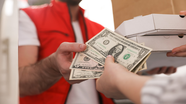 person handing cash tip to pizza store employee