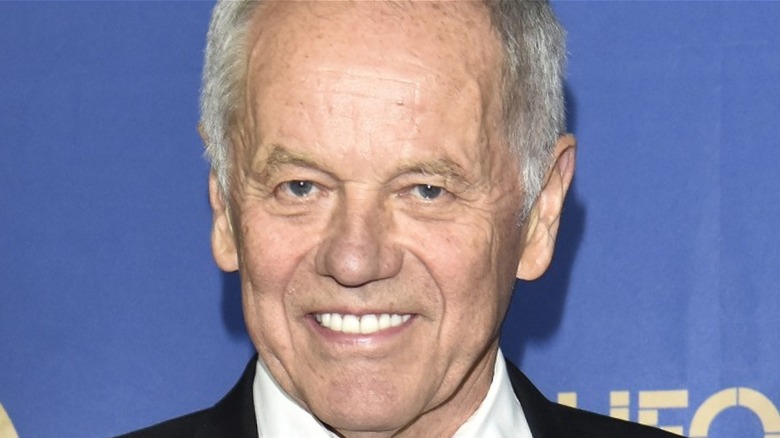 Wolfgang Puck smiles in a white shirt and black suit